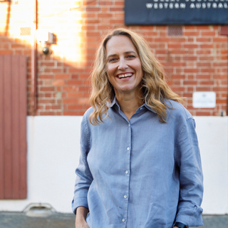 Woman in a blue shirt standing outdoors with a brick wall and wooden door in the background