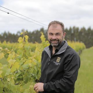 Man standing in a vineyard wearing a branded jacket.