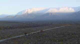 Scenic view of a mountain range with clouds and a road in the foreground.