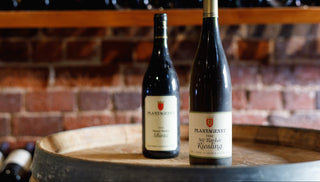 Two wine bottles on a wooden barrel with a brick wall background