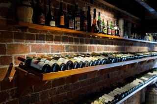 Row of wine bottles on wooden shelves against a brick wall.