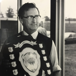 Man wearing a formal vest with a prominent emblem, standing indoors.